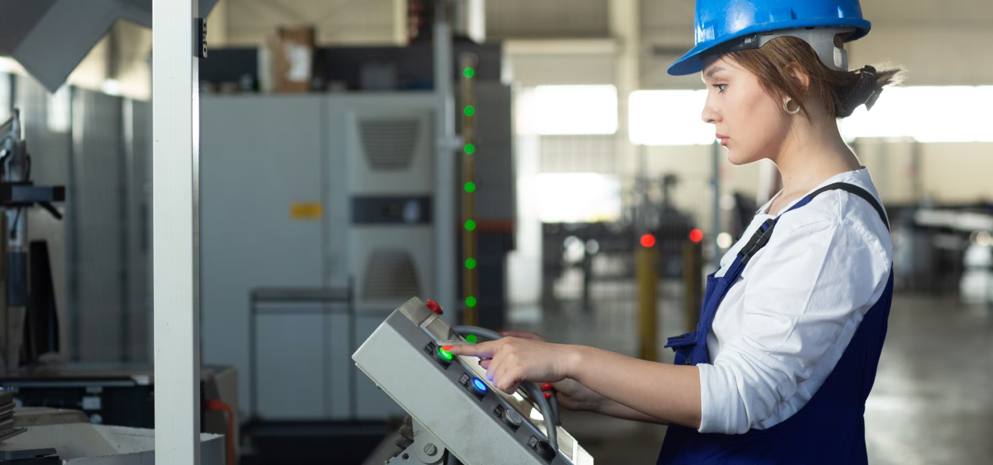 Opératrice portant un casque bleu et utilisant le pupitre de commande d’une machine industrielle.