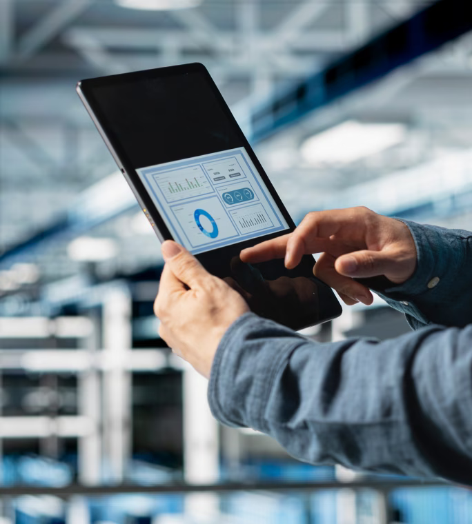Personne consultant des graphiques et des indicateurs sur une tablette dans un atelier industriel.