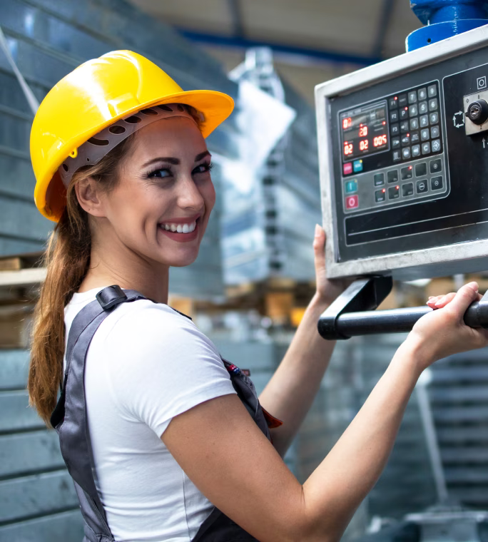 Opératrice portant un casque jaune à côté du panneau de commande d’une machine industrielle.
