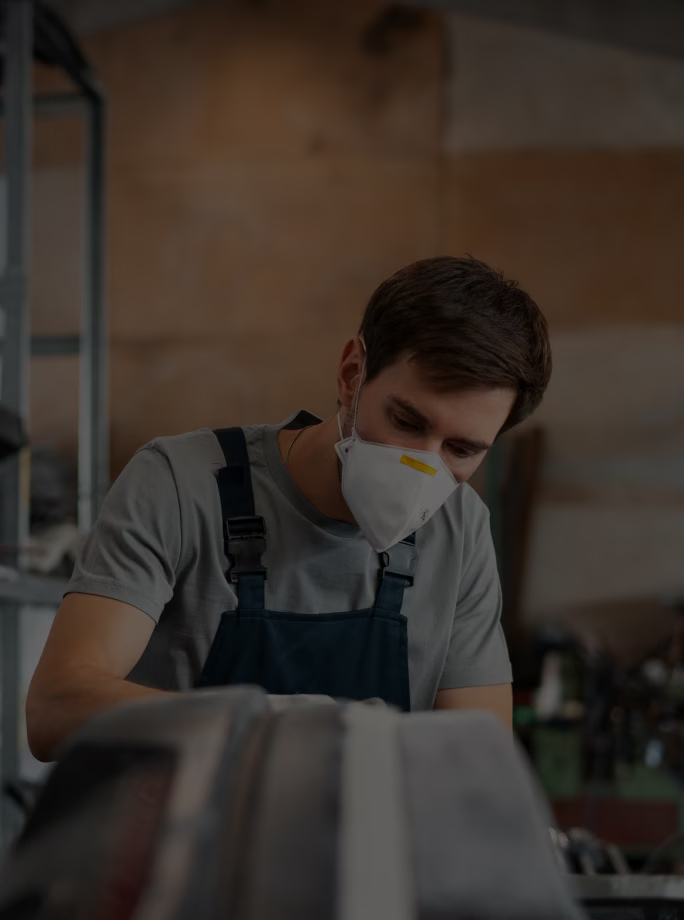 Opérateur équipé d’un masque contrôlant une pièce dans un atelier de fabrication.