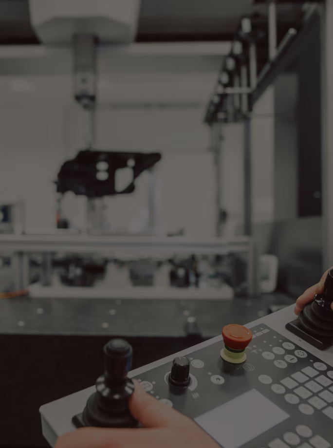 Gros plan sur des mains manipulant les joysticks d’un pupitre de commande devant une machine industrielle.