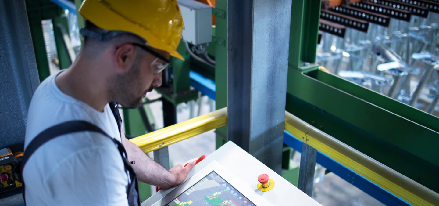 Opérateur utilisant l’écran tactile d’un pupitre de contrôle devant une installation industrielle.