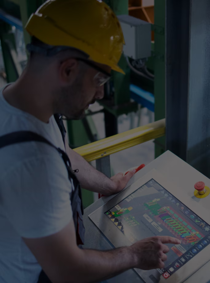 Opérateur portant un casque jaune et utilisant l’écran tactile d’un pupitre de contrôle industriel.