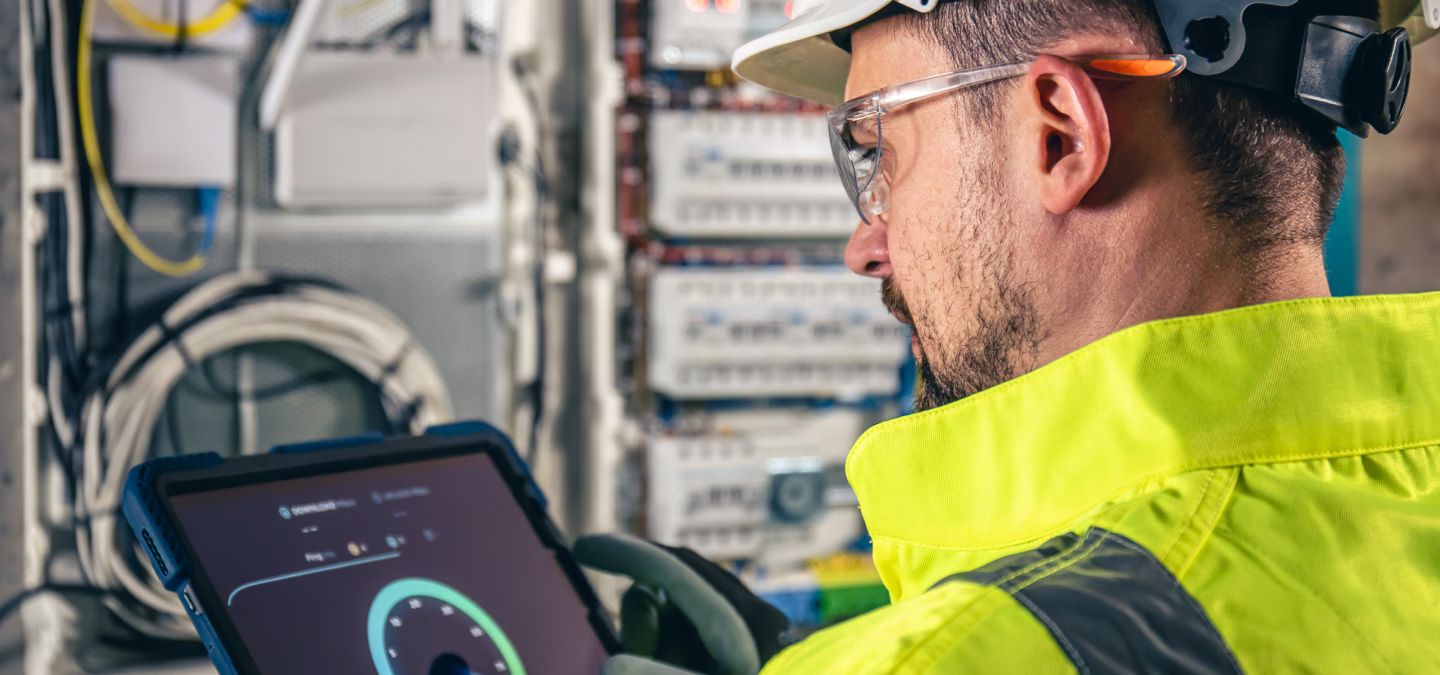 Technicien en tenue haute visibilité consultant une tablette devant une armoire électrique ouverte.
