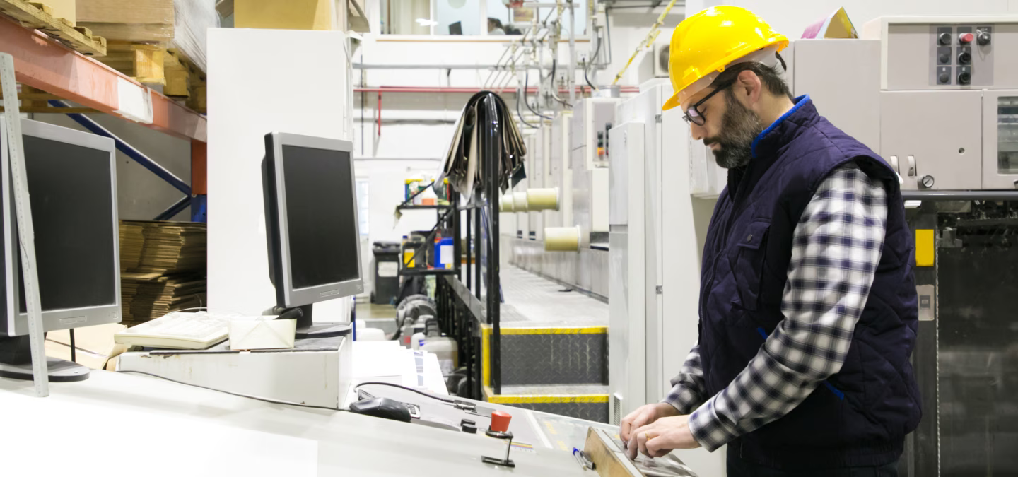 Opérateur portant un casque jaune et utilisant un pupitre dans un atelier équipé d’écrans.